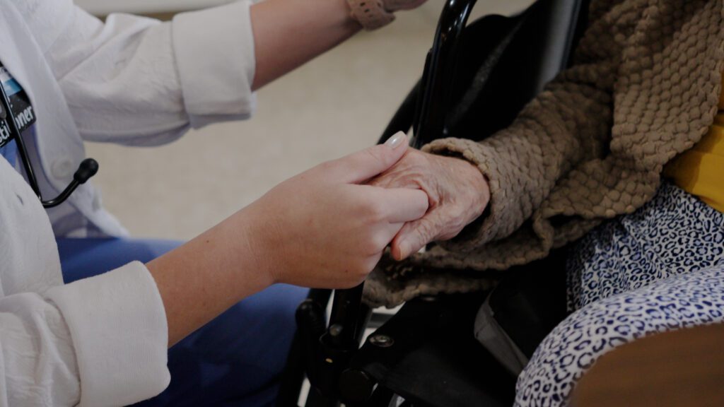 A nurse holds hands with a memory care resident at a skilled nursing facility