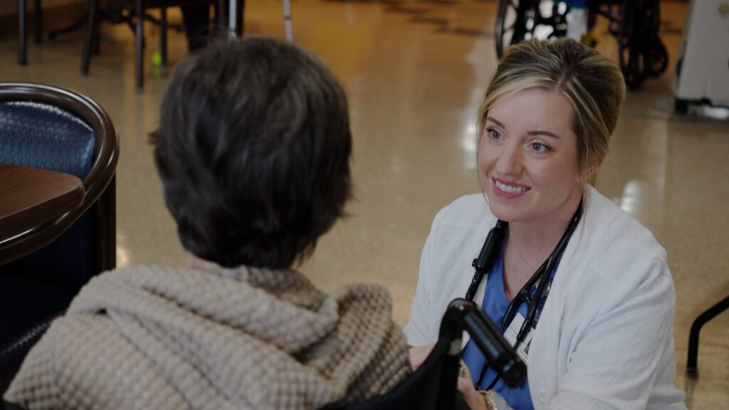 A nurse smiles at a resident at a skilled nursing nursing home