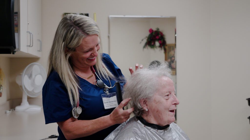A stylist smiles while doing a resident's hair